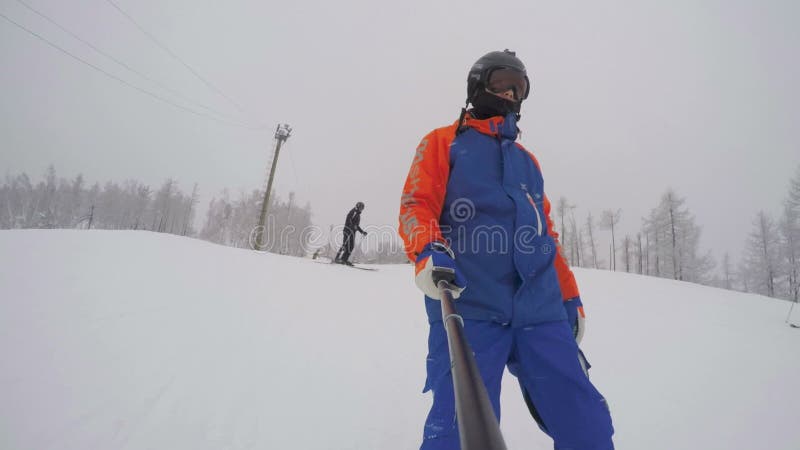 Een sneeuwboarder daalt van een berg nabij een skier tijdens een zware sneeuwval