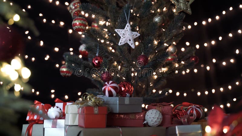 Een stapel kleurrijke cadeaudozen onder de kerstboom en versiering met bokeh - lampen in de woonkamer bij nacht