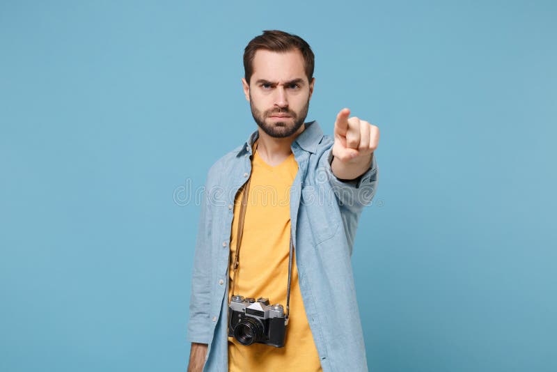 Strict traveler tourist man in yellow summer clothes with photo camera isolated on blue background. Male passenger traveling abroad on weekends Air flight journey concept Point index finger on camera. Strict traveler tourist man in yellow summer clothes with photo camera isolated on blue background. Male passenger traveling abroad on weekends Air flight journey concept Point index finger on camera