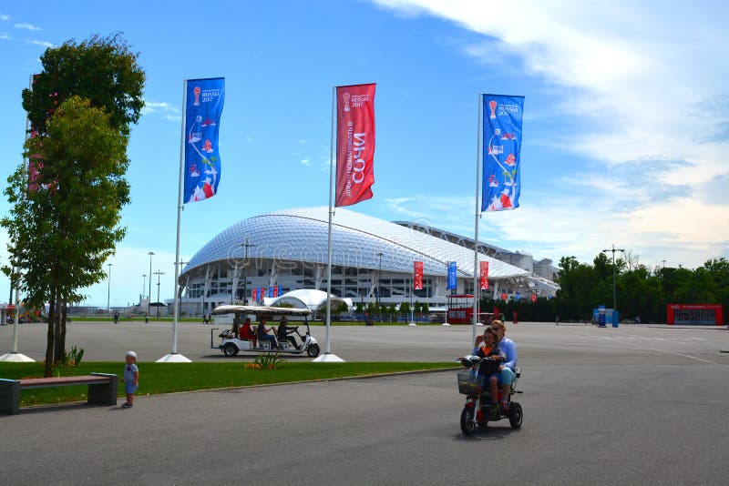 Een toeristen elektrische auto en een familie op een elektrische fiets op de achtergrond van het stadion van ` Fisht ` stock foto's Een toeristen elektrische auto en een familie op een elektrische fiets op de achtergrond van het stadion van ` Fisht ` stock foto's