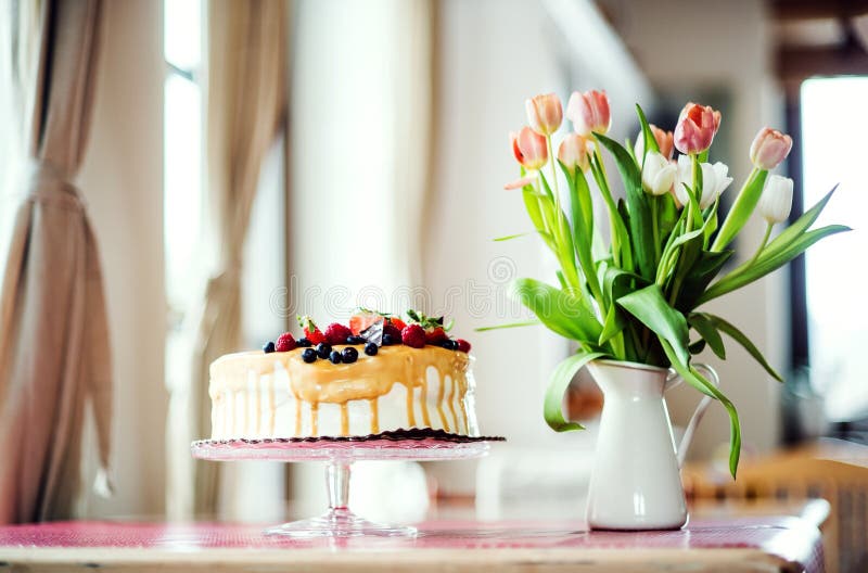 Een verjaardagscake op een glastribune en een vaas met tulpen op de lijst stock afbeeldingen Een verjaardagscake op een glastribune en een vaas met tulpen op de lijst stock afbeeldingen