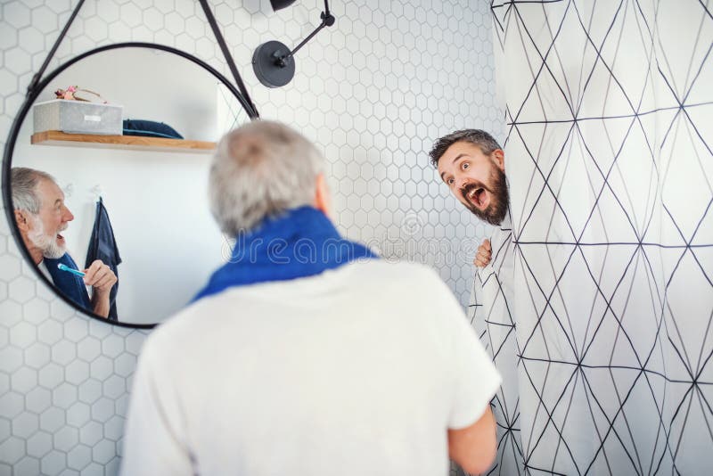 Een volwassen hipsterzoon en een hogere vader in badkamers binnen thuis, hebbend pret royalty-vrije stock foto Een volwassen hipsterzoon en een hogere vader in badkamers binnen thuis, hebbend pret royalty-vrije stock foto