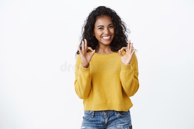 Cheerful pleased dark-skinned girl student in yellow sweater smiling with approval and delight, show okay good gesture, rate excellent promo, recommend great app, looking satisfied, white background. Cheerful pleased dark-skinned girl student in yellow sweater smiling with approval and delight, show okay good gesture, rate excellent promo, recommend great app, looking satisfied, white background.