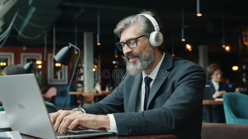 Een vrolijke kantoormedewerker die een laptop gebruikt in café om muziek te luisteren en te zingen in restaurant
