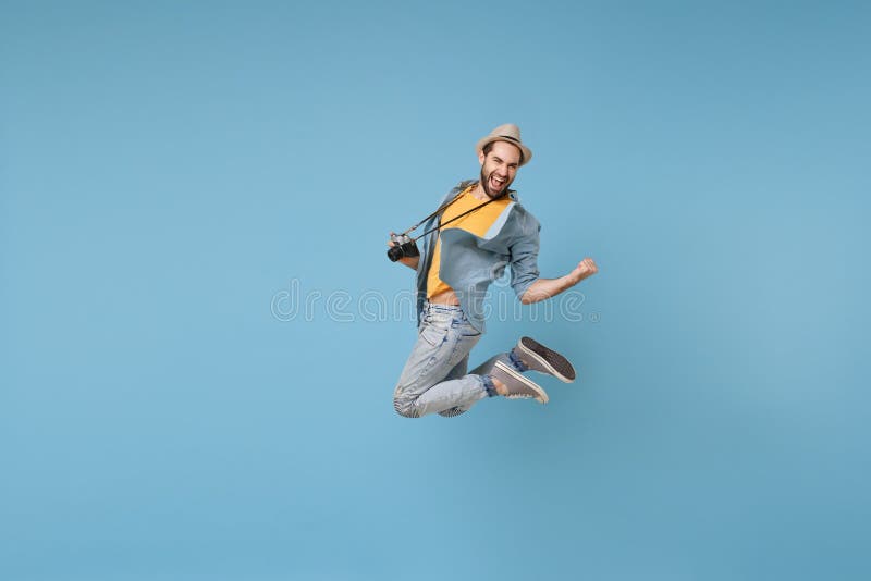 Joyful traveler tourist man in yellow casual clothes with photo camera isolated on blue background. Male passenger traveling abroad on weekend. Air flight journey concept Jumping doing winner gesture. Joyful traveler tourist man in yellow casual clothes with photo camera isolated on blue background. Male passenger traveling abroad on weekend. Air flight journey concept Jumping doing winner gesture