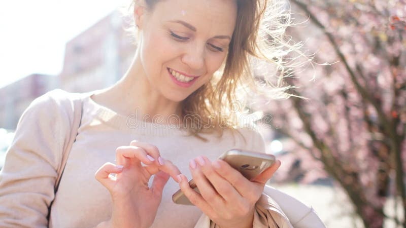 Een vrouw bekijkt het scherm van haar smartphone Het meisje typt SMS en glimlacht terwijl status in het midden van stock videobeelden Een vrouw bekijkt het scherm van haar smartphone Het meisje typt SMS en glimlacht terwijl status in het midden van stock videobeelden