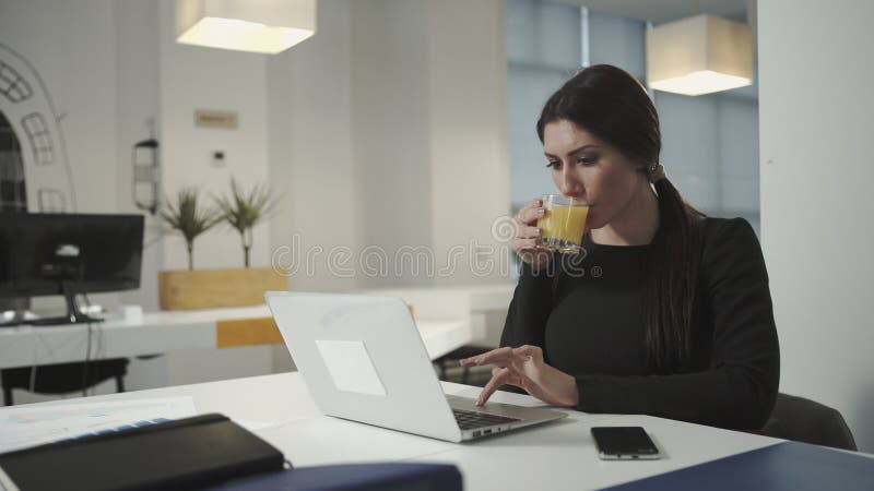 Een vrouw die bij het de computer en het drinken jus d'orange werken