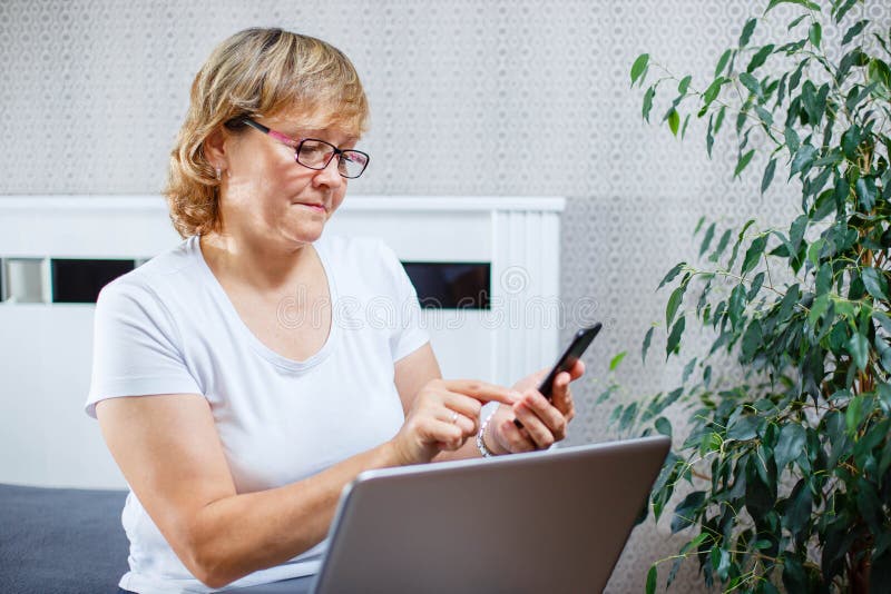 Een vrouw die op middelbare leeftijd online het winkelen doen gebruikend een smartphone en laptop royalty-vrije stock afbeeldingen Een vrouw die op middelbare leeftijd online het winkelen doen gebruikend een smartphone en laptop royalty-vrije stock afbeeldingen