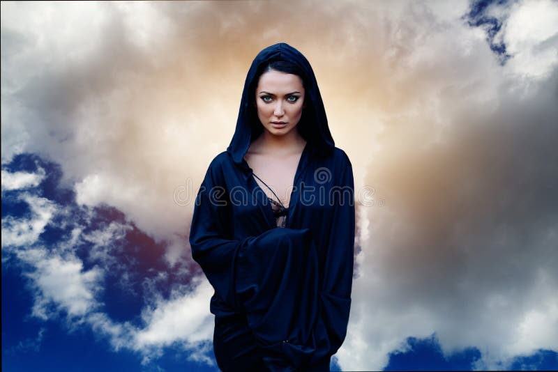 Een vrouw is een helderziendetovenaar en een prediker in een zwarte mystieke mantel met een kap tegen een dramatische achtergrond royalty-vrije stock foto Een vrouw is een helderziendetovenaar en een prediker in een zwarte mystieke mantel met een kap tegen een dramatische achtergrond royalty-vrije stock foto