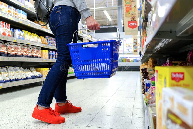 Een vrouw houdt het handvat van de kruidenierswinkelkar, die onderaan de doorgang in de supermarkt gaan Koop het product Heilige- royalty-vrije stock afbeeldingen Een vrouw houdt het handvat van de kruidenierswinkelkar, die onderaan de doorgang in de supermarkt gaan Koop het product Heilige- royalty-vrije stock afbeeldingen