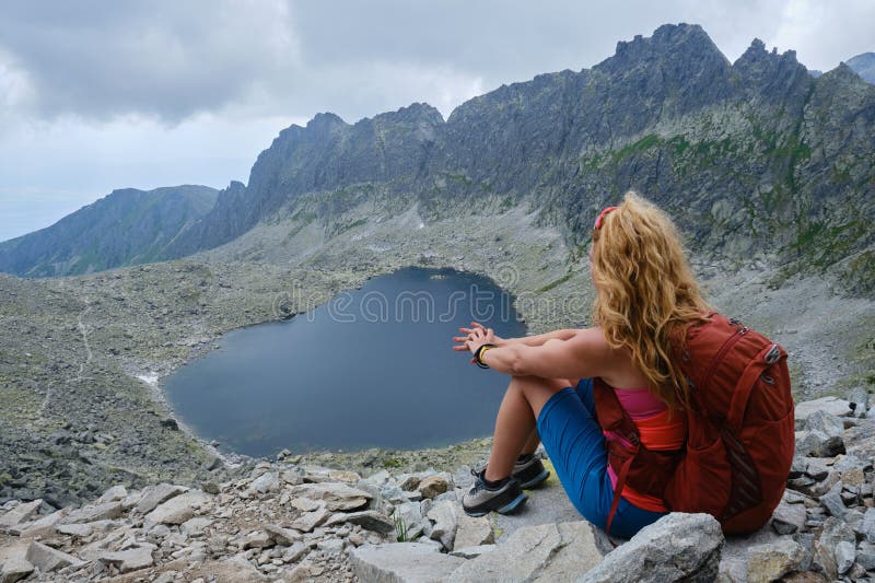 Een vrouw met een krullenhaar en een rode rugzak kijkt naar het vysne wahlenbergovo meer in slowakije met hoge tatras - bergen.