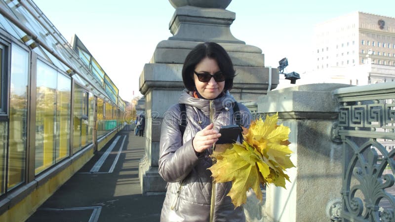 Een vrouw van middelbare leeftijd een ' brunette caucasian race ' met een boeket gele bladeren loopt over de brug en schrijft sms