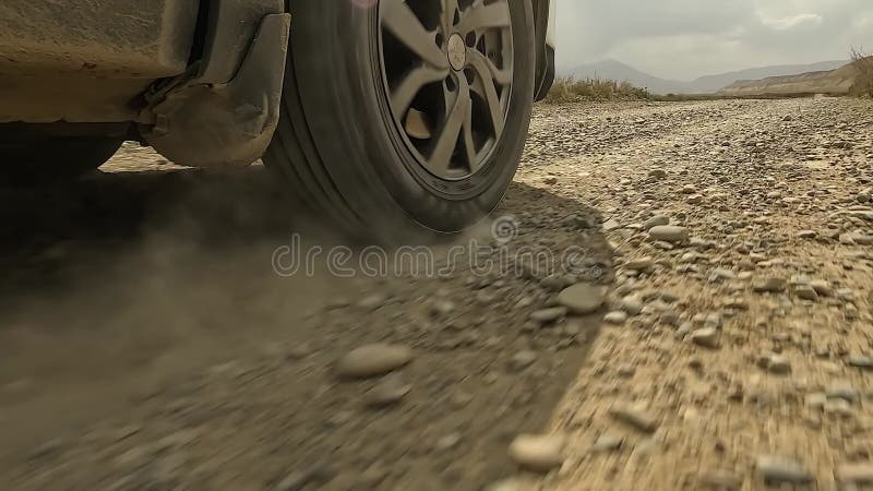 Een vuile auto rijdt op een rotsachtige weg die stof doet ontstaan. de overgang van het rechterachterwiel van de auto naar de voor