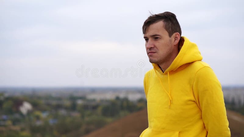 Een weldenkende man in gele hoodie ziet er uit op hilarisch terrein. ernstig mannetje dat op het platteland in gedachten is verlor