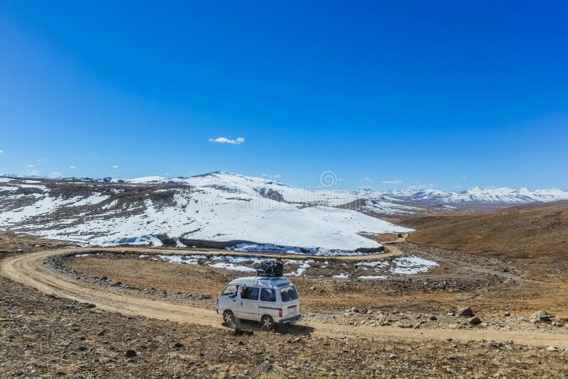 Een witte bestelwagen met bagage op het dak die langs de ongeplaveide weg lopen stock foto Een witte bestelwagen met bagage op het dak die langs de ongeplaveide weg lopen stock foto