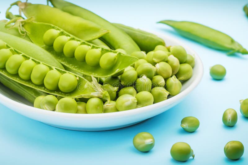 Een witte die plaat met peulen en erwten van groene erwten wordt gevuld In de nadruk is een open peul royalty-vrije stock afbeelding Een witte die plaat met peulen en erwten van groene erwten wordt gevuld In de nadruk is een open peul royalty-vrije stock afbeelding