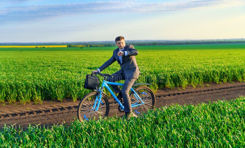 Een zakenman rijdt een fiets met een aktetas en controleert zijn polshorloge op een groen grijs veld dat in een pak is gekleed