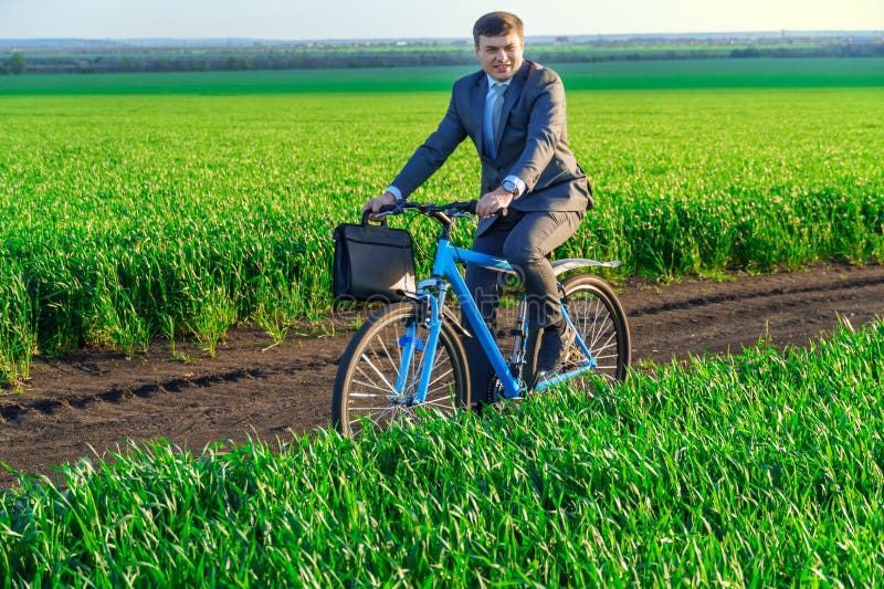 Een zakenman rijdt een fiets met een aktetas op een groen grijs veld , dat in het voorjaar is gekleed in een mooi bedrijfspak