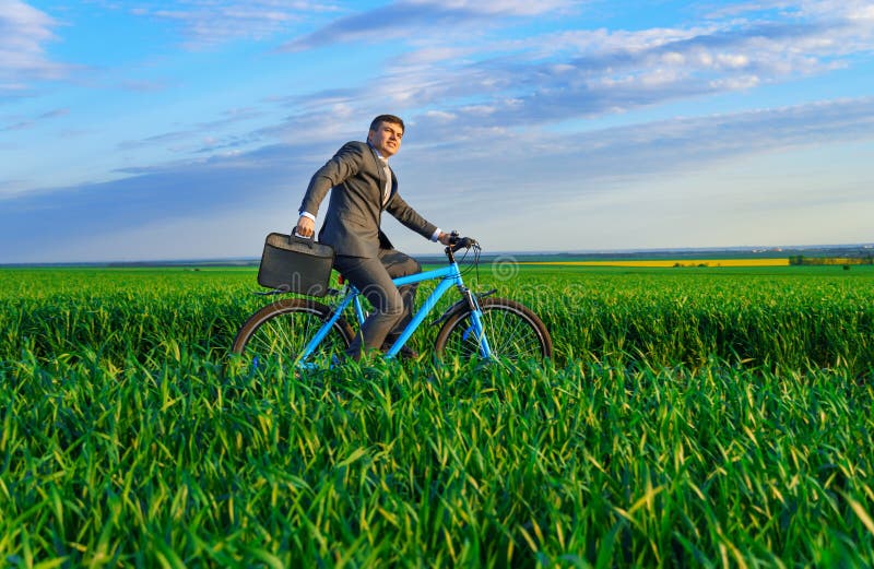 Een zakenman rijdt een fiets met een aktetas op een groen grijs veld , dat in het voorjaar is gekleed in een mooi bedrijfspak