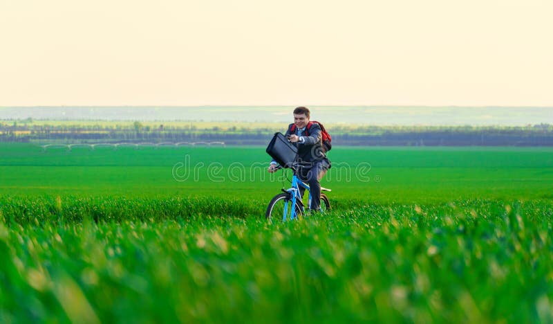 Een zakenman rijdt een fiets met een rugzak en een aktetas op een groen grijs veld dat is gekleed in een mooi pak