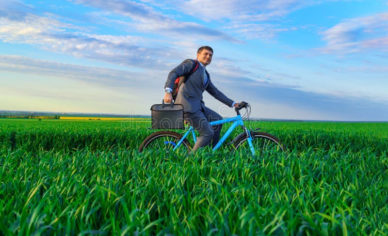 Een zakenman rijdt een fiets met een rugzak en een aktetas op een groen grijs veld dat is gekleed in een mooi pak