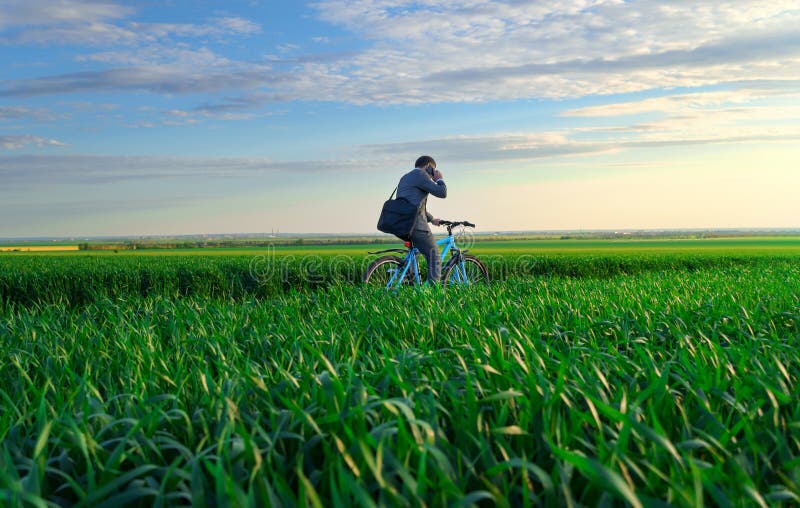Een zakenman rijdt een fiets op een groen grijs veld in een business suit die hij aantrekt vanuit een mooie natuur in