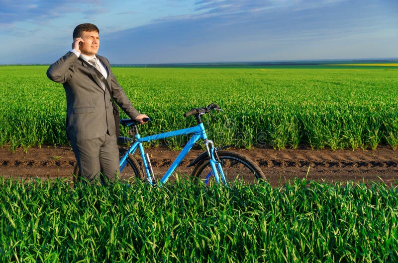 Een zakenman rijdt een fiets op een groen grijs veld in een business suit die hij aantrekt vanuit een mooie natuur in