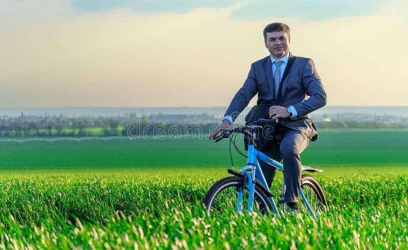 Een zakenman rijdt een fiets op een groen grijsveld , gekleed in een mooi pak , in een lente freelance business .
