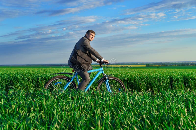 Een zakenman rijdt een fiets op een groen grijsveld , gekleed in een mooi pak , in een lente freelance business .