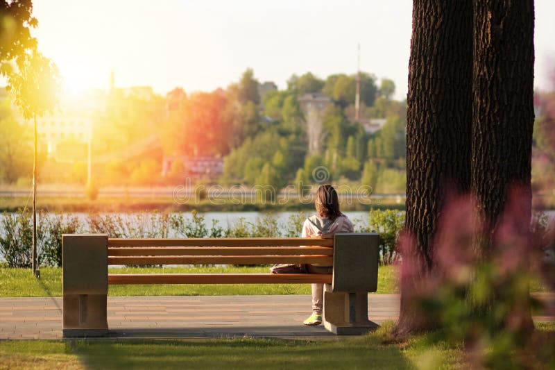 Eenzame jonge vrouwenzitting op een bank in het park dichtbij het meer op zonsondergang stock afbeeldingen Eenzame jonge vrouwenzitting op een bank in het park dichtbij het meer op zonsondergang stock afbeeldingen