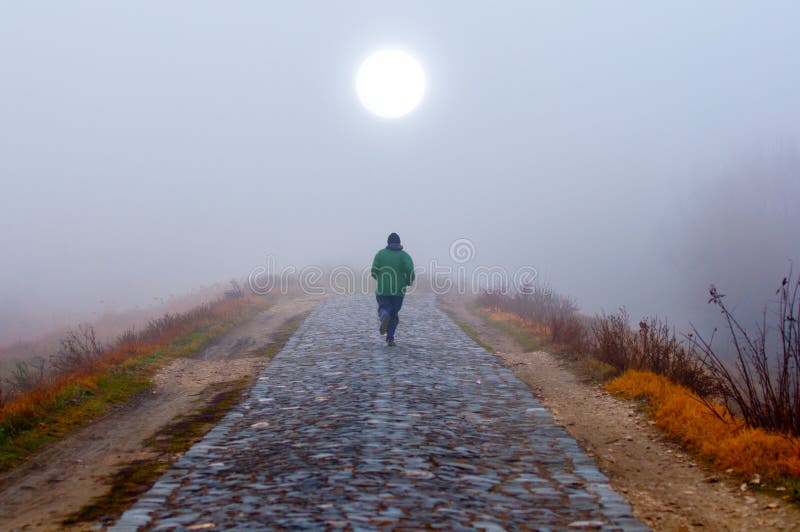 Eenzame mens die naar de zon op nevelige ochtend loopt royalty-vrije stock fotografie Eenzame mens die naar de zon op nevelige ochtend loopt royalty-vrije stock fotografie