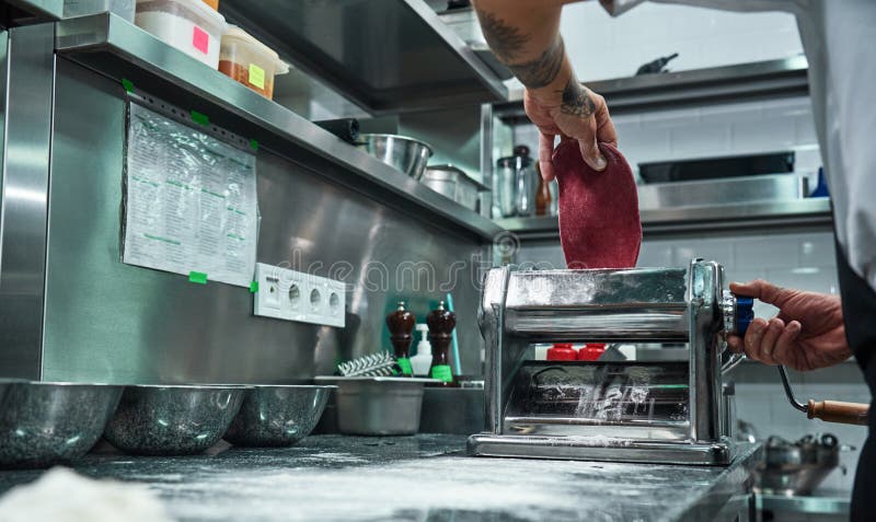 Effectuer des pâtes L'image cultivée du roulement masculin de chef malaxent par la machine de pâtes tout en travaillant dans la c images stock Effectuer des pâtes L'image cultivée du roulement masculin de chef malaxent par la machine de pâtes tout en travaillant dans la c images stock