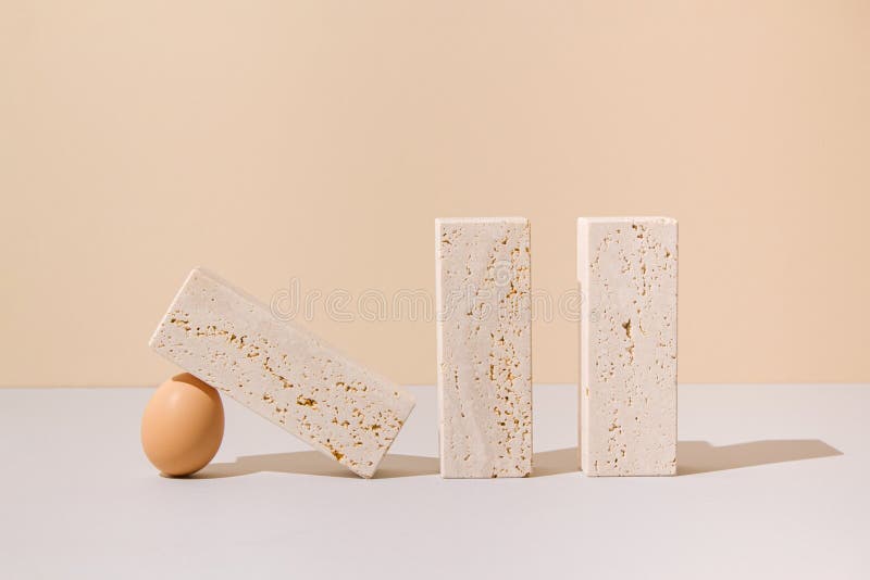 Egg holding a travertine marble block on a beige and gray background. 2021 Easter unique still life concept. stock images