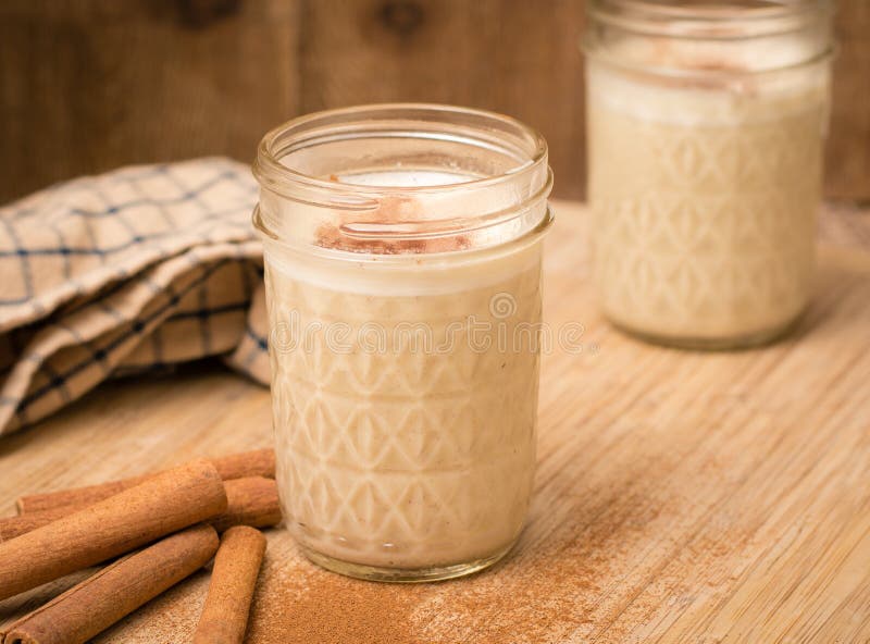 Quilted mason jar with egg nog. Cinnamon sticks are laying at the base with rustic setting. Quilted mason jar with egg nog. Cinnamon sticks are laying at the base with rustic setting.