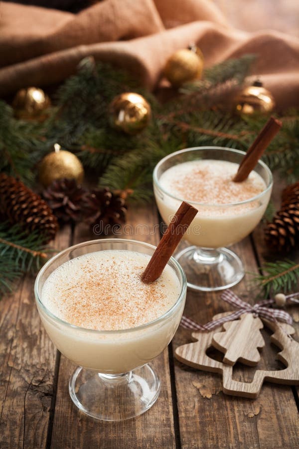 Eggnog traditional homemade egg, milk, rum, vanilla alcohol liqueur preparation recipe in two glass cups with cinnamon sticks on wooden vintage table. Shallow depth of field