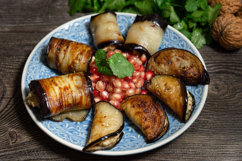 Eggplant and pepper rolls with walnut stuffing on a blue plate with pomegranate seeds. Georgian food. 8 servings, garnished with stock photos Eggplant and pepper rolls with walnut stuffing on a blue plate with pomegranate seeds. Georgian food. 8 servings, garnished with stock photos