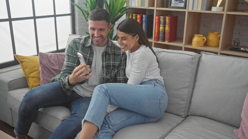 Ehepaar, das sich auf einem Sofa im gemütlichen Wohnzimmer mit Blick auf ein Telefon amüsiert lizenzfreie stockfotos