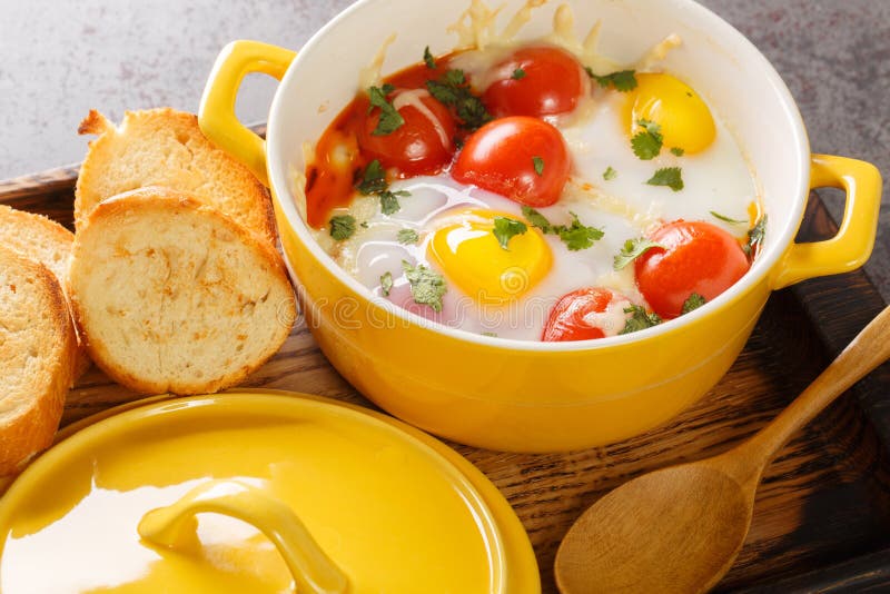 Eggs en Cocotte with cream and cheese served with warm toast for dipping closeup in the wooden tray on the table. Horizontal. Eggs en Cocotte with cream and cheese served with warm toast for dipping closeup in the wooden tray on the table. Horizontal