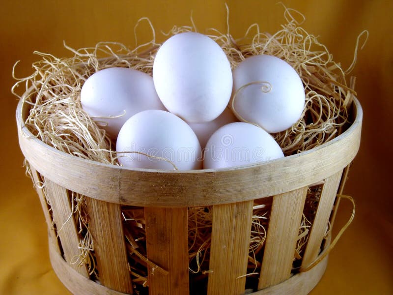 Six white eggs resting in shredded excelsior in a slatted, wooden basket. Six white eggs resting in shredded excelsior in a slatted, wooden basket.