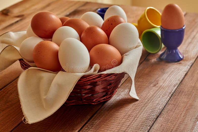 Eieren in rieten mand en eierdopjes op lijst stock afbeeldingen Eieren in rieten mand en eierdopjes op lijst stock afbeeldingen
