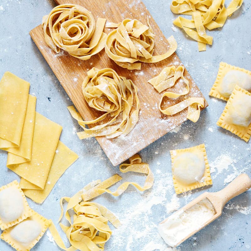 Homemade italian pasta, ravioli, fettuccine, tagliatelle on a wooden board and on a blue background. The cooking process, raw pasta. Tasty raw ravioli with ricotta and spinach,with flour on background. Homemade italian pasta, ravioli, fettuccine, tagliatelle on a wooden board and on a blue background. The cooking process, raw pasta. Tasty raw ravioli with ricotta and spinach,with flour on background