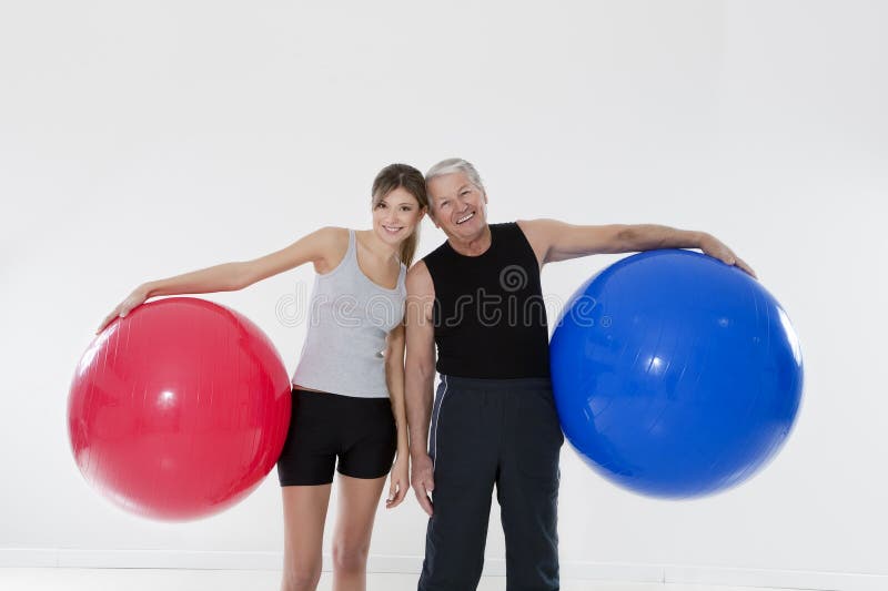 Senior adult and daughter exercising with fitness ball in gym. Senior adult and daughter exercising with fitness ball in gym