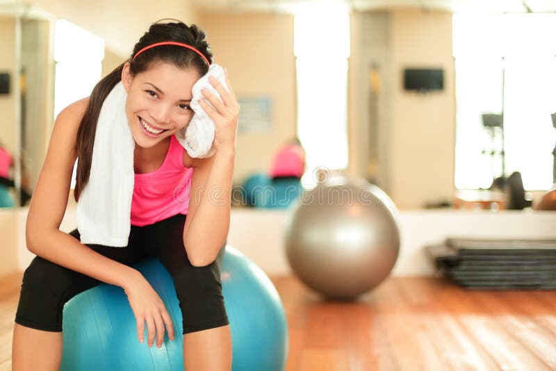 Fitness woman in gym resting on pilates ball / exercise ball sweating using towel relaxing after training. Beautiful multiracial fitness model in gym. Fitness woman in gym resting on pilates ball / exercise ball sweating using towel relaxing after training. Beautiful multiracial fitness model in gym.