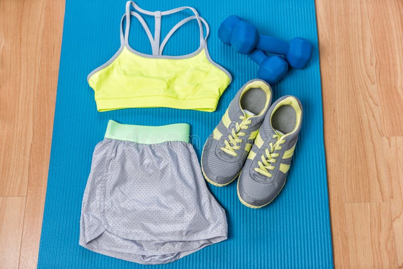 Eignungsausstattung auf Übungsmatte mit Gewichten und Laufschuhen Sport-BH und graue kurze Hosen für zu Hause ausbilden Art und M stockfotografie Eignungsausstattung auf Übungsmatte mit Gewichten und Laufschuhen Sport-BH und graue kurze Hosen für zu Hause ausbilden Art und M stockfotografie
