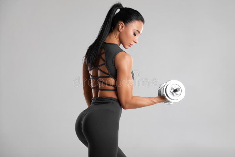 Fitness woman doing exercise for biceps on gray background. Muscular woman workout with dumbbells. Fitness woman doing exercise for biceps on gray background. Muscular woman workout with dumbbells.