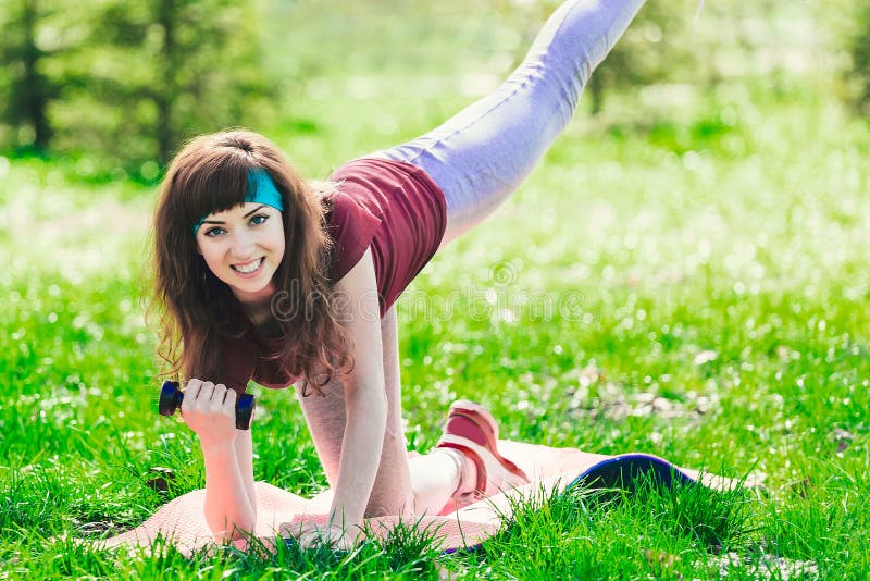 Eignungsmädchen im Park und in den verschiedenen Übungen mit Dummkopf und Matte engagiert Brunette strebt herein Sport draußen an lizenzfreie stockfotografie Eignungsmädchen im Park und in den verschiedenen Übungen mit Dummkopf und Matte engagiert Brunette strebt herein Sport draußen an lizenzfreie stockfotografie