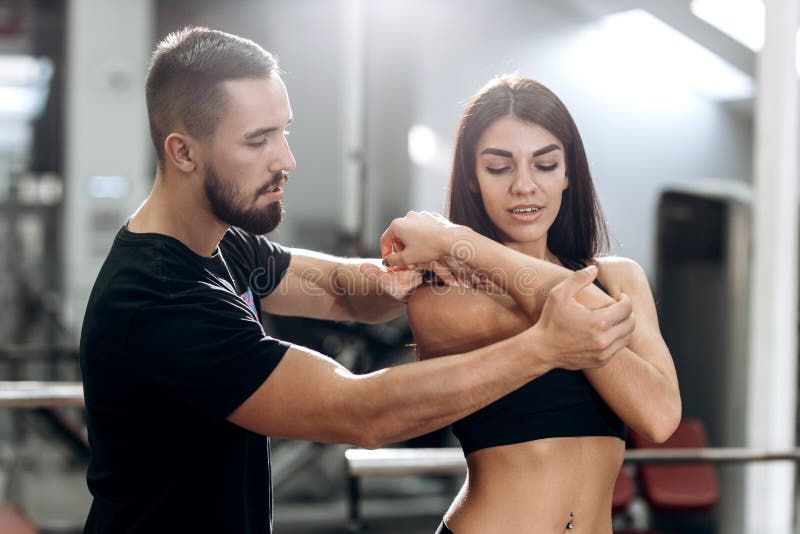 Eignungstrainer explans zum athletischen Mädchen gekleidet in der schwarzen Sportkleidung, wie Muskeln der Arme bearbeitet stockbild