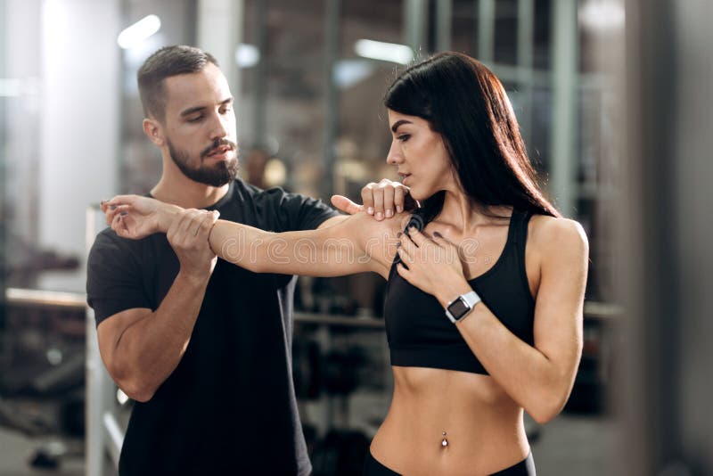 Eignungstrainer explans zum athletischen Mädchen gekleidet in der schwarzen Sportkleidung, wie Muskeln der Arme bearbeitet lizenzfreies stockbild