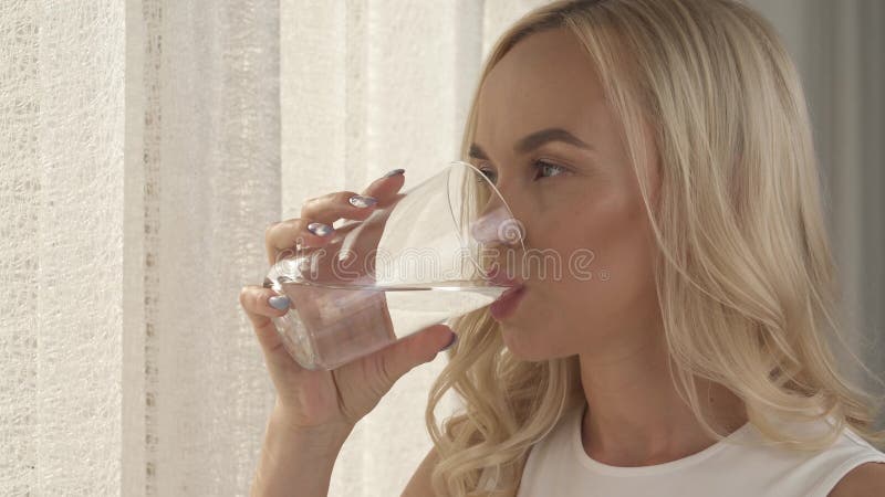 Ein Abschluss oben von womanâ€™s Hand, die ein Glas Wasser hält die Kamera schiebt hoch Eine Seitenansicht hübschen blondeâ€™s Ge