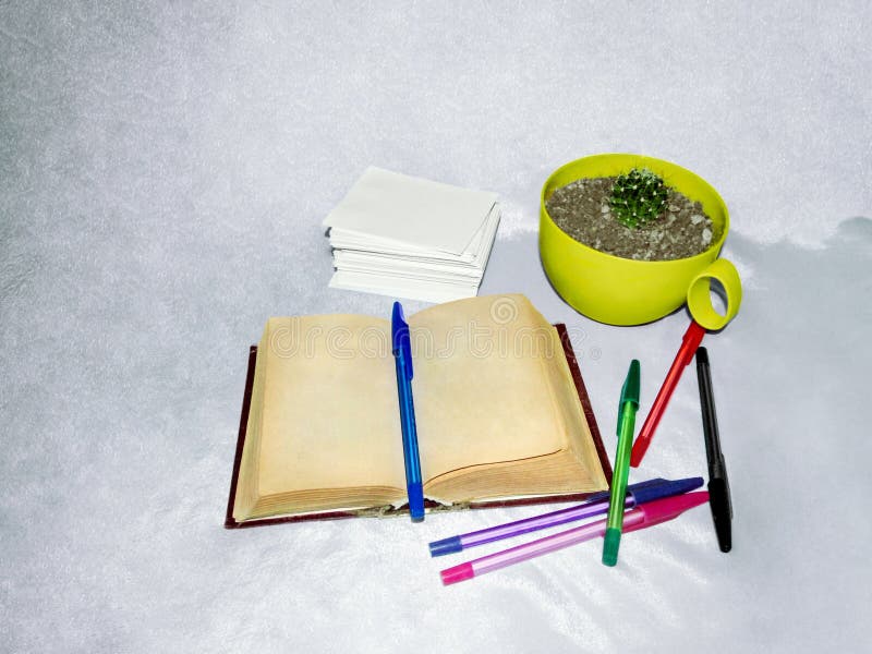 Ein altes Buch mit gelb gefärbten Seiten, mehrfarbigen Stiften, einem Stapel Weißbuch und Kaktus lizenzfreie stockfotografie Ein altes Buch mit gelb gefärbten Seiten, mehrfarbigen Stiften, einem Stapel Weißbuch und Kaktus lizenzfreie stockfotografie